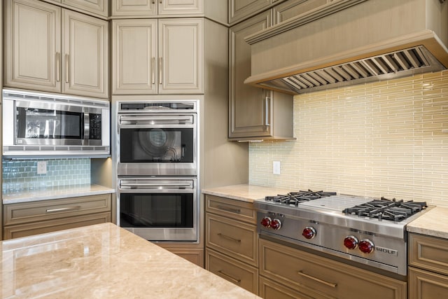 kitchen featuring light stone countertops, backsplash, stainless steel appliances, and custom exhaust hood