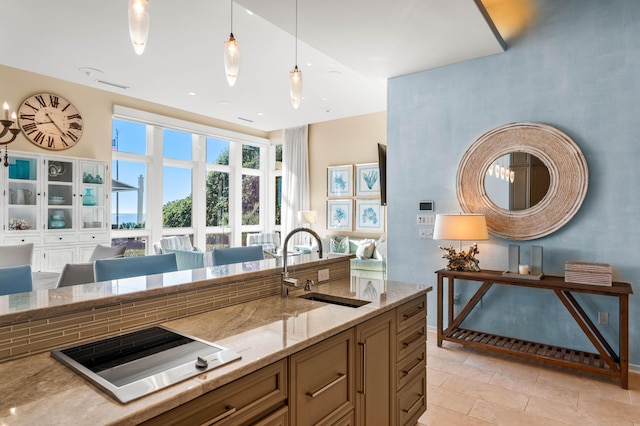 kitchen featuring sink, cooktop, light stone counters, decorative light fixtures, and light tile patterned floors