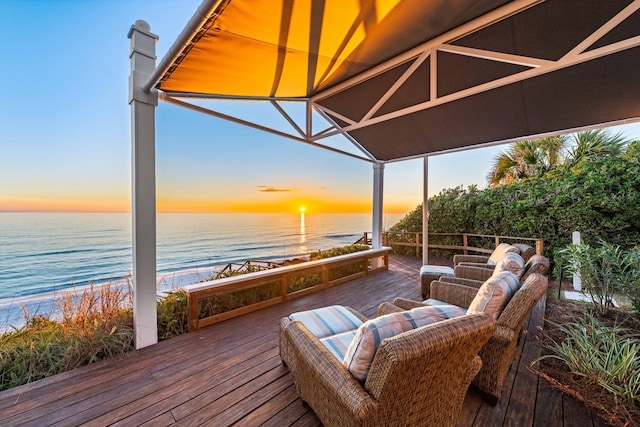 deck at dusk featuring an outdoor living space, a water view, and a beach view