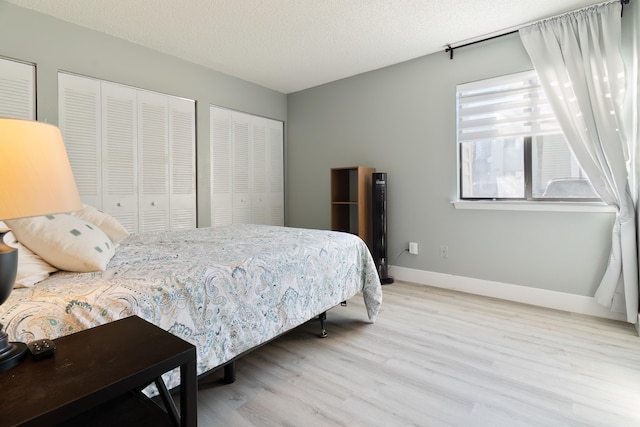 bedroom featuring a textured ceiling, light wood-type flooring, and two closets