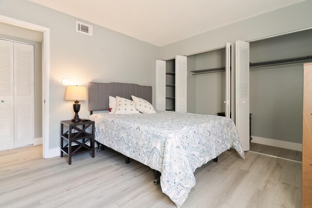 bedroom with light hardwood / wood-style floors and two closets