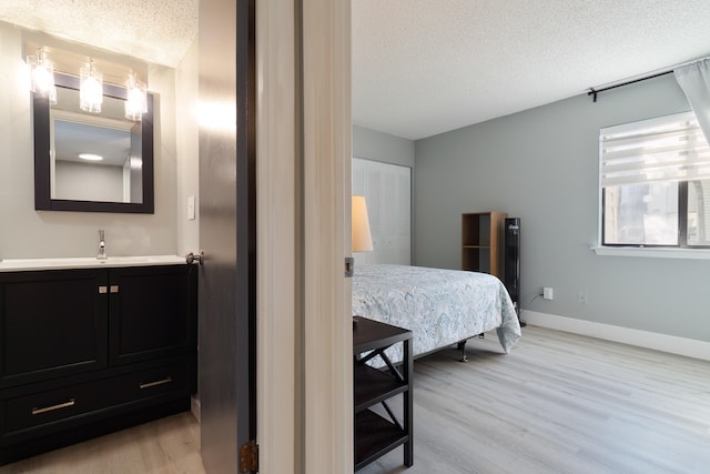 bedroom featuring a textured ceiling, a closet, sink, and light hardwood / wood-style floors