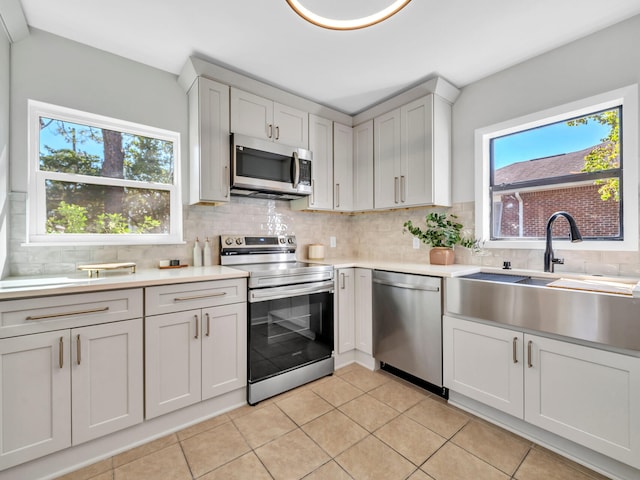 kitchen featuring stainless steel appliances, white cabinets, tasteful backsplash, sink, and light tile patterned floors