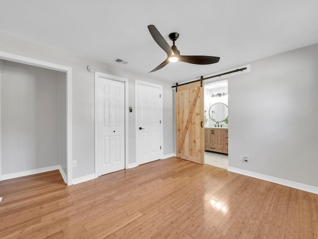 unfurnished bedroom with light wood-type flooring, ceiling fan, a barn door, and connected bathroom