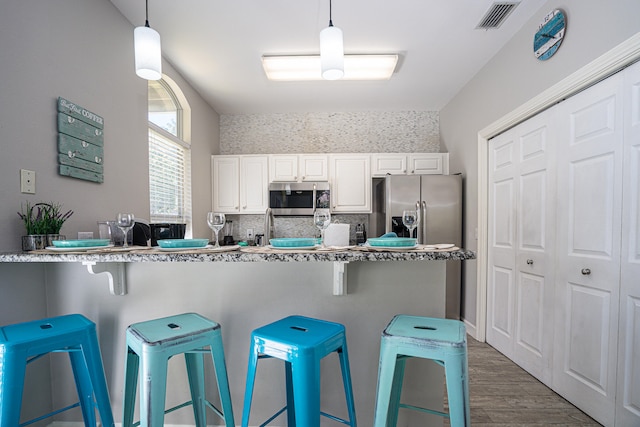 kitchen featuring white cabinets, hanging light fixtures, a kitchen bar, dark wood-type flooring, and stainless steel appliances