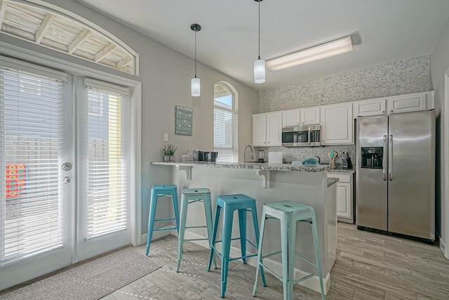 kitchen featuring white cabinetry, light stone counters, appliances with stainless steel finishes, and a breakfast bar area