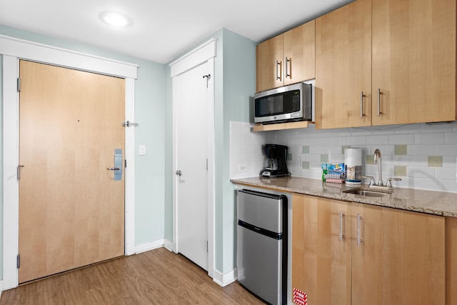 kitchen featuring light stone counters, tasteful backsplash, sink, light hardwood / wood-style floors, and appliances with stainless steel finishes