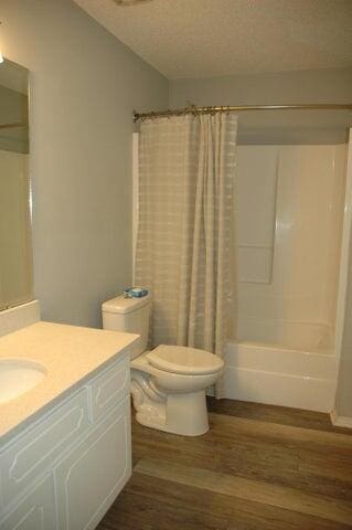 full bathroom with vanity, hardwood / wood-style flooring, shower / bath combo with shower curtain, toilet, and a textured ceiling