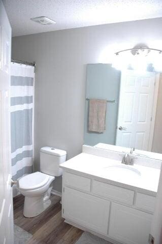 bathroom with walk in shower, toilet, wood-type flooring, vanity, and a textured ceiling