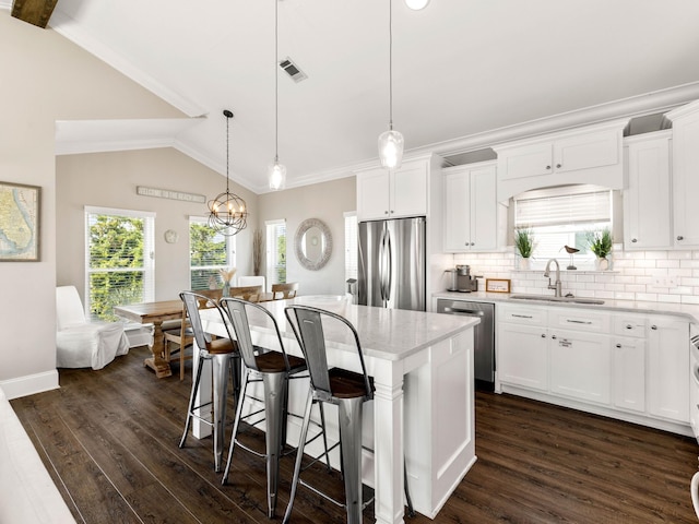 kitchen with a kitchen island, stainless steel appliances, vaulted ceiling, pendant lighting, and white cabinets