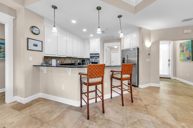 kitchen with kitchen peninsula, stainless steel appliances, a kitchen bar, white cabinets, and tasteful backsplash