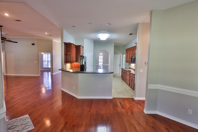 kitchen with kitchen peninsula, black fridge, hardwood / wood-style floors, and ceiling fan