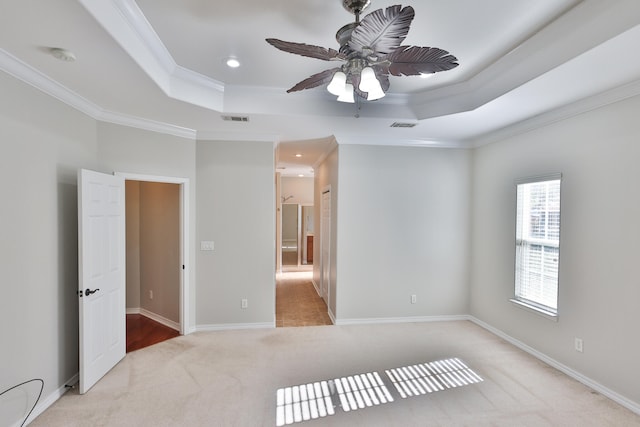 empty room featuring ornamental molding, light carpet, ceiling fan, and a tray ceiling