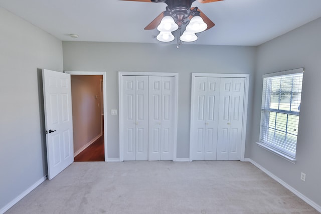 unfurnished bedroom with ceiling fan, two closets, and light colored carpet