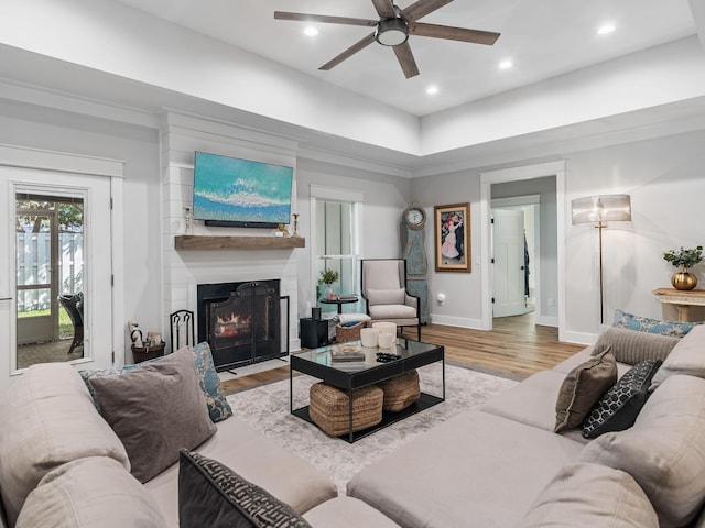 living room with hardwood / wood-style floors, ceiling fan, a large fireplace, and crown molding