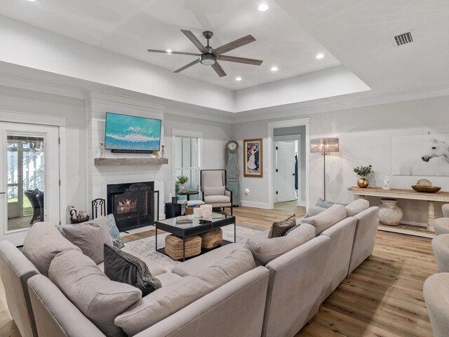 living room with a raised ceiling, ceiling fan, a large fireplace, and light wood-type flooring