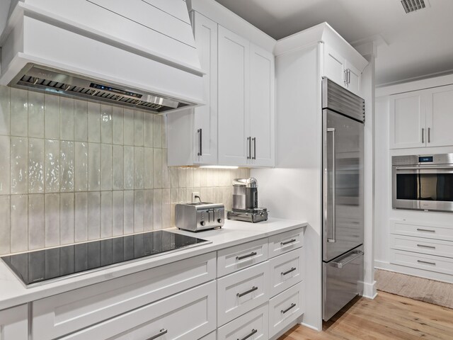 kitchen featuring white cabinets, light wood-type flooring, stainless steel appliances, and range hood