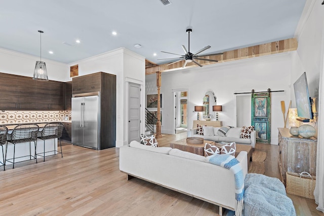 living room featuring light hardwood / wood-style flooring, a barn door, ceiling fan, and crown molding