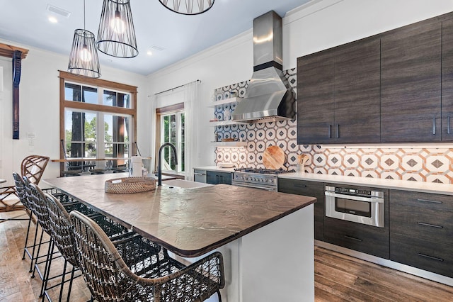 kitchen featuring decorative backsplash, a center island with sink, a breakfast bar, wall chimney exhaust hood, and sink