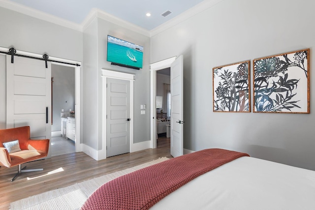 bedroom with ensuite bathroom, a barn door, hardwood / wood-style flooring, and crown molding