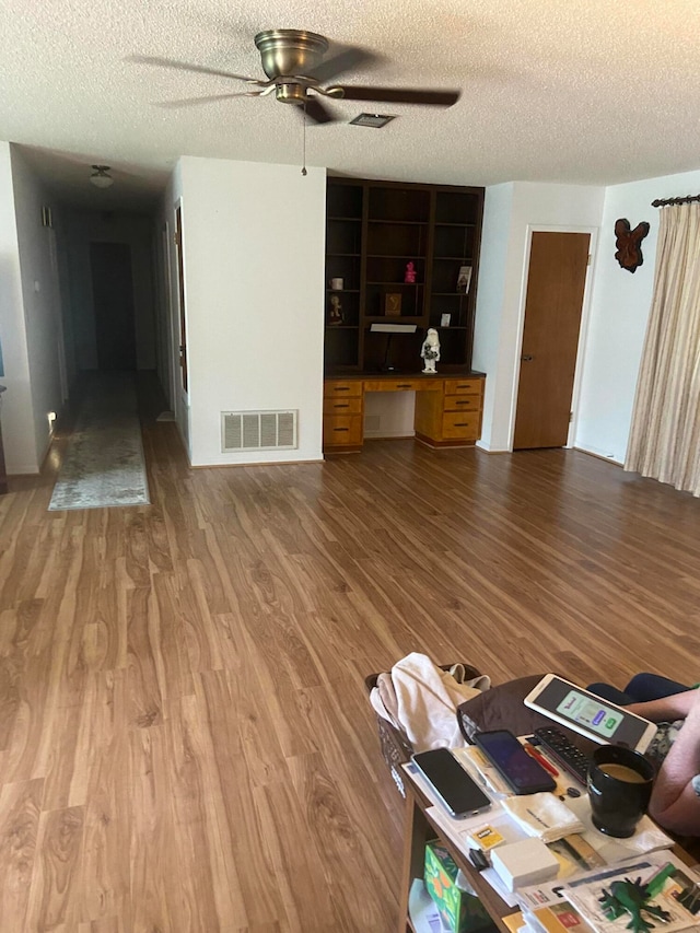 unfurnished living room with hardwood / wood-style floors, built in desk, and a textured ceiling