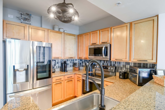 kitchen featuring tasteful backsplash, light brown cabinets, sink, stainless steel appliances, and light stone countertops