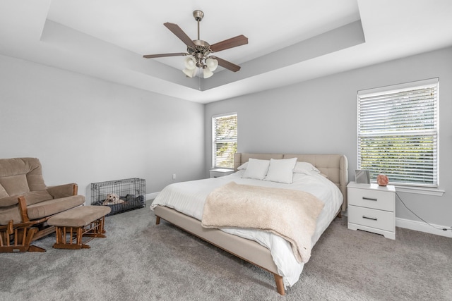 carpeted bedroom featuring a tray ceiling, baseboards, and ceiling fan