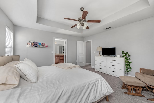 bedroom featuring a tray ceiling, connected bathroom, carpet, and ceiling fan