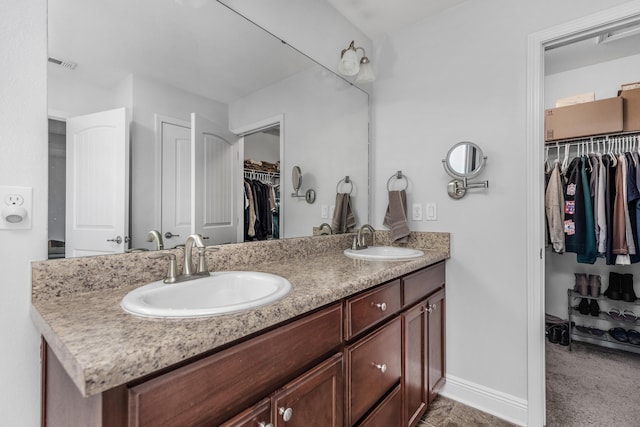 full bathroom with double vanity, a spacious closet, and baseboards