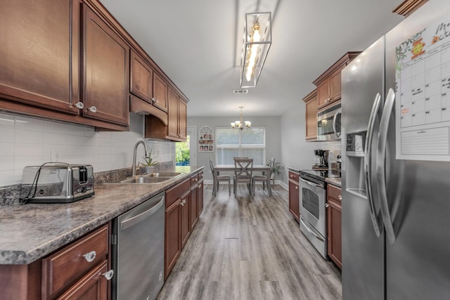 kitchen featuring appliances with stainless steel finishes, a sink, backsplash, light wood-type flooring, and a chandelier