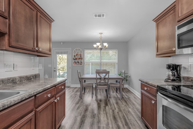 kitchen with light hardwood / wood-style floors, decorative light fixtures, a notable chandelier, decorative backsplash, and appliances with stainless steel finishes