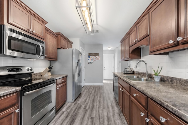 kitchen with appliances with stainless steel finishes, a sink, baseboards, light wood finished floors, and backsplash