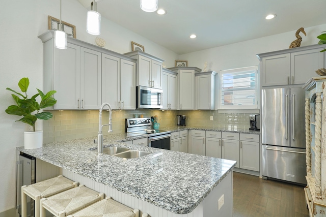 kitchen featuring kitchen peninsula, decorative light fixtures, stainless steel appliances, dark hardwood / wood-style floors, and a kitchen bar