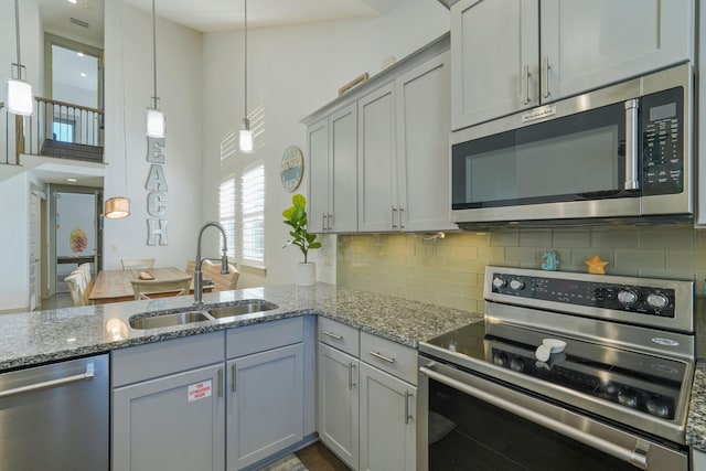 kitchen with sink, gray cabinetry, decorative light fixtures, stone counters, and appliances with stainless steel finishes