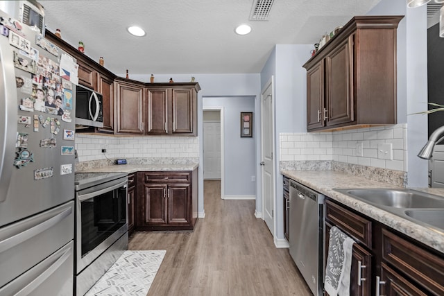 kitchen featuring dark brown cabinets, stainless steel appliances, tasteful backsplash, and light hardwood / wood-style flooring