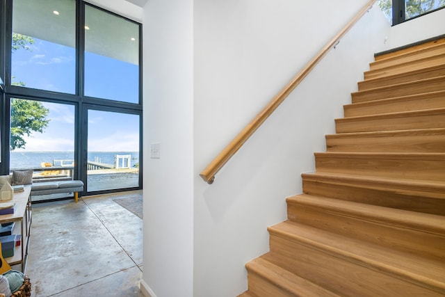 staircase with a water view, concrete flooring, and a high ceiling