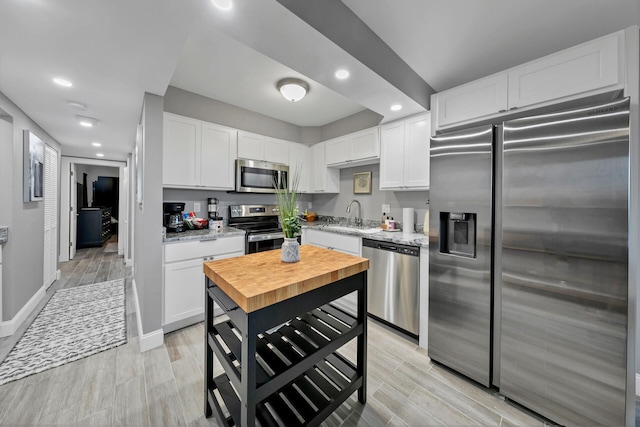 kitchen with butcher block counters, sink, stainless steel appliances, light hardwood / wood-style floors, and white cabinets