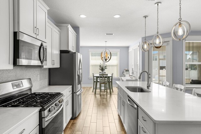 kitchen with sink, an island with sink, white cabinetry, stainless steel appliances, and pendant lighting