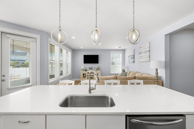 kitchen featuring white cabinets, hanging light fixtures, sink, and a kitchen island with sink