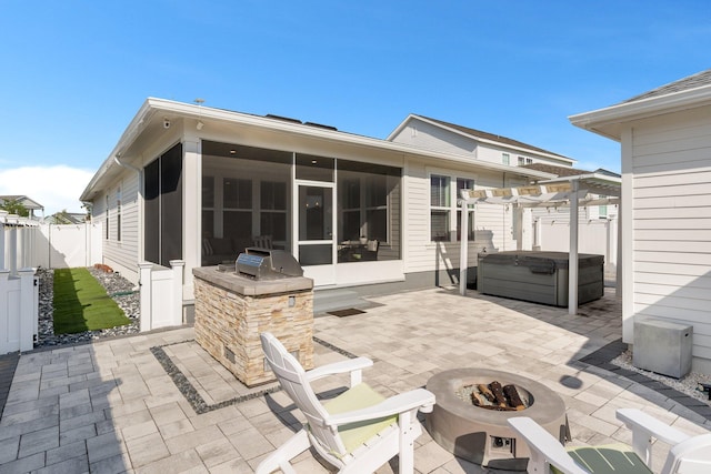 rear view of house with area for grilling, a hot tub, a patio area, a sunroom, and an outdoor fire pit