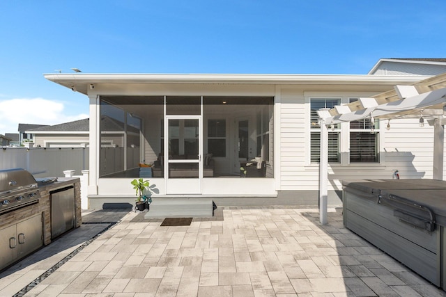 view of patio / terrace with a hot tub, an outdoor kitchen, area for grilling, and a sunroom