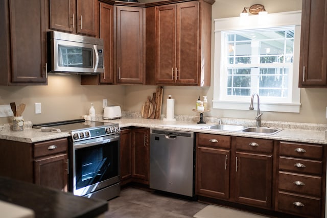 kitchen with sink, light stone countertops, dark brown cabinets, and stainless steel appliances