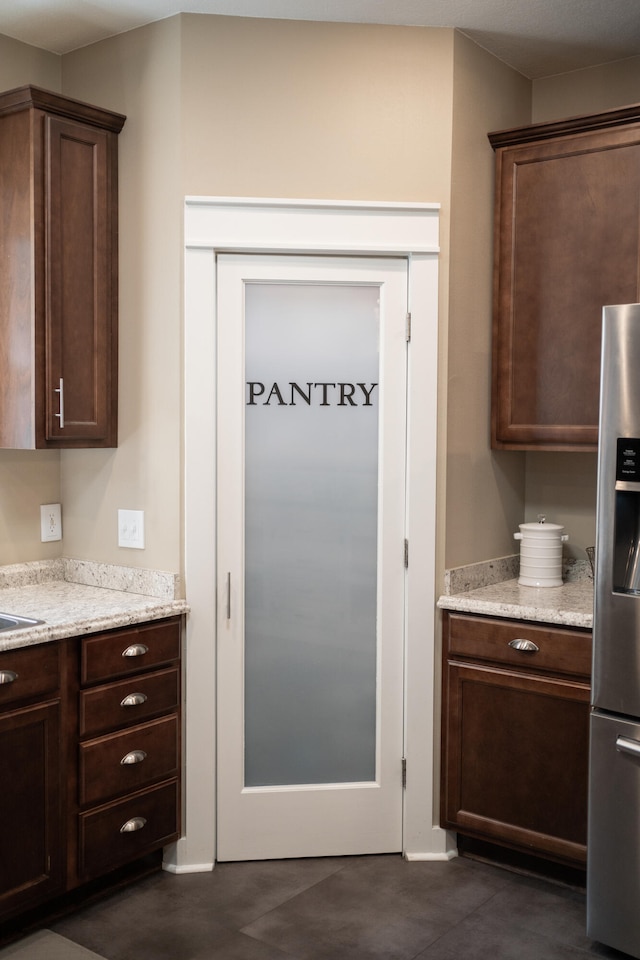 kitchen with light stone counters, dark brown cabinets, and stainless steel fridge with ice dispenser