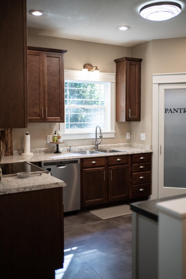 kitchen featuring stainless steel dishwasher, sink, light stone countertops, and dark brown cabinetry