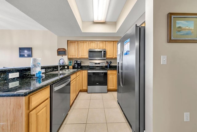 kitchen with dark stone countertops, sink, kitchen peninsula, appliances with stainless steel finishes, and light tile patterned floors