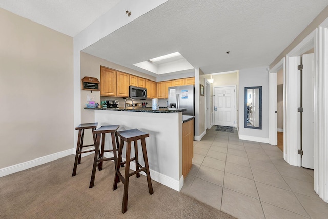 kitchen with light tile patterned flooring, kitchen peninsula, a kitchen bar, and a textured ceiling