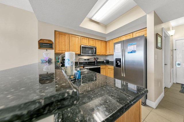 kitchen featuring stainless steel appliances, kitchen peninsula, light tile patterned floors, and dark stone counters