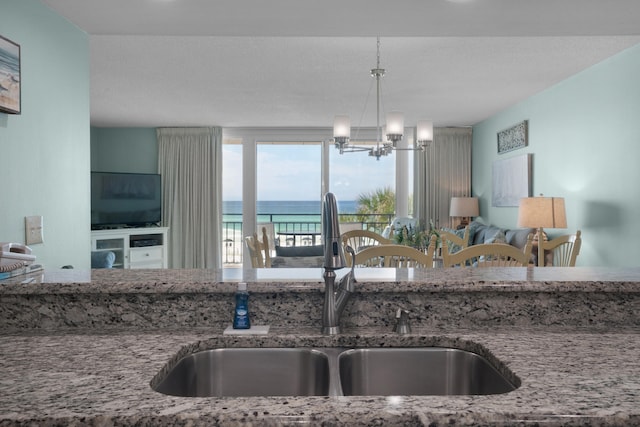 kitchen with stone countertops, a notable chandelier, decorative light fixtures, and sink