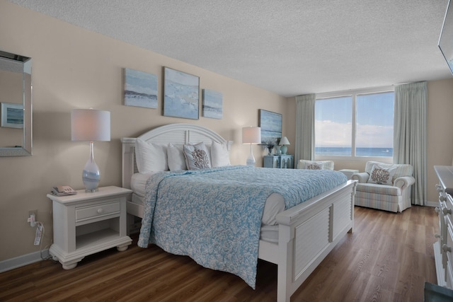 bedroom with a water view, dark hardwood / wood-style floors, and a textured ceiling