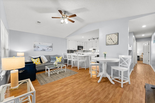 living area with visible vents, a ceiling fan, light wood finished floors, and vaulted ceiling